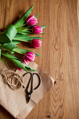 Floristic workplace with craft paper, twine Arranging pink tulips bouquet on wooden table