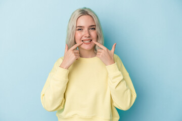 Young caucasian woman isolated on blue background smiles, pointing fingers at mouth.