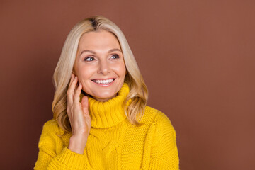 Fototapeta na wymiar Photo of curious sweet blond elder lady look empty space wear yellow sweater isolated on brown color background
