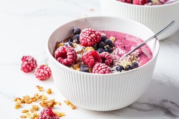 Berry smoothie bowl with granola, coconut and hemp seeds, marble background. Vegan food concept.