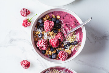 Berry smoothie bowl with granola, coconut and hemp seeds, marble background. Vegan food concept.