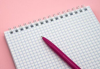 Notepad and pen on pink. Pink Pen. A blank checkered sheet of paper. Notepad spring Spiral spiral checked sheets.
