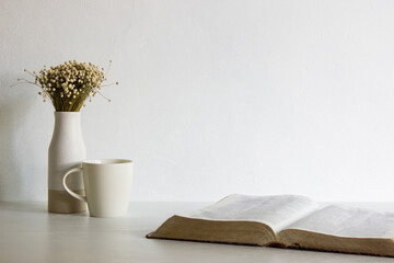 Book with coffee and flowers on table with nature light. 