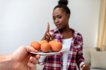 Cropped shot of young African-American woman refusing to eat eggs. Young beautiful woman holding...