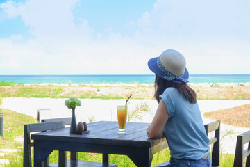 Asia woman drinking orange juice on table near tropical seaside