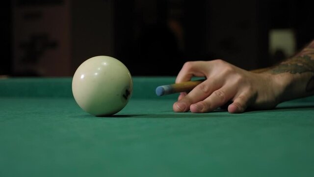 Close-up of a man hitting a billiard ball with a cue that stands on a table with a green cloth.