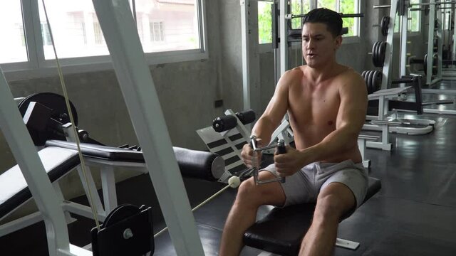 fit man shirtless exercises with  rowing machine in fitness club  . Muscular man workout  pumping up muscles chest with cable crossover at gym . bodybuilder training in sport center