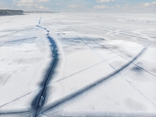 Aerial drone top view of snow covered frozen lake or river surface with big cracked ice diagonal lines. Natural winter landscape abstract texture pattern. Dangerous pond melting at thaw season