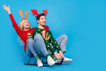 Photo of impressed funny young people wear ugly ornament pullovers riding sledges looking empty...