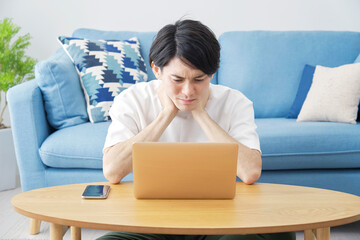 部屋でパソコンを使う男性　不安の表情