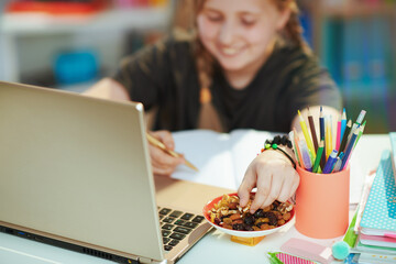 Smiling girl having online education and eating healthy snack