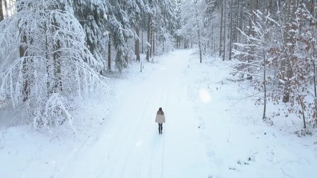 Epic drone footage looking down at the snow covered trees and a lonely girl walking at sunset