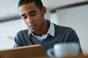 Serious young Black man engrossed in reading on a tablet pc