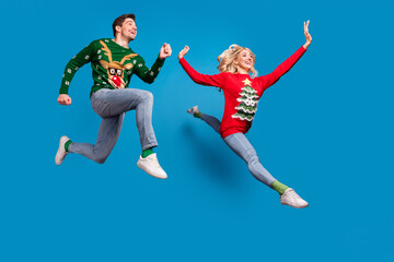 Fototapeta na wymiar Photo of positive pretty young couple dressed ugly print sweaters smiling jumping high running fast isolated blue color background