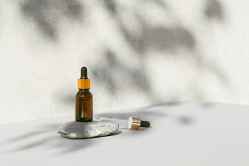 Amber glass bottle of essential oil or serum with pipette on stone podium with grey concrete wall with shadows as a background. Natural skincare cosmetic concept