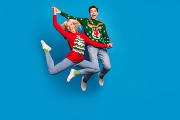 Photo of sweet good mood young people wear ugly ornament pullovers jumping high dancing isolated blue color background