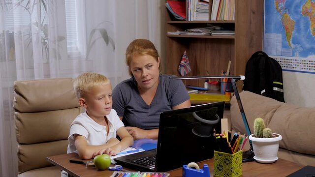 A happy mother and her son are talking to a teacher during an online video chat lesson on distance learning, the boy raises his hand to answer a question. Homeschooling during the coronavirus pandemic