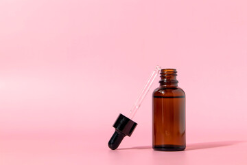 Brown glass bottle with dropper on pink background. Serum or essential oil packaging. Mockup of a cosmetic product. Front view with copy space.