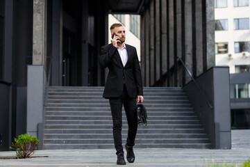 A Banker In A Stylish Suit With A Cell Phone And A Briefcase In His Hand Goes Down The Stairs On The Street To Meet With Investors. Business Concept Photo