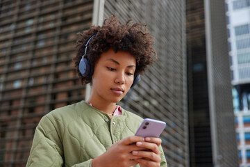 Beautiful millennial girl enjoys favorite song in headphones connected to smarphone via bluetooth...