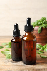 Bottles of basil essential oil and green leaves on wooden table