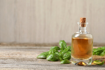 Glass bottle of basil essential oil and leaves on wooden table. Space for text
