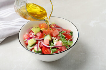 Adding olive oil to delicious salad with watermelon, vegetables and feta cheese at light table