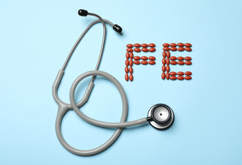 Pills and stethoscope on light blue background, flat lay. Anemia concept