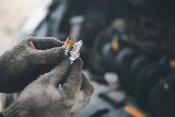 Spark plug replacement work, Hand of the auto mechanic holding the old spark plug on blurred engine...