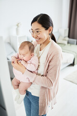 Asian woman holding her baby standing in the room and showing reflection in the mirror
