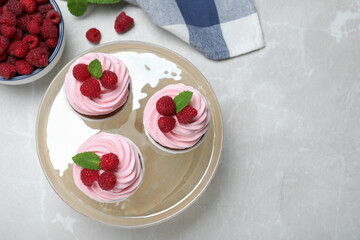 Delicious cupcakes with cream and raspberries on light grey marble table, flat lay. Space for text