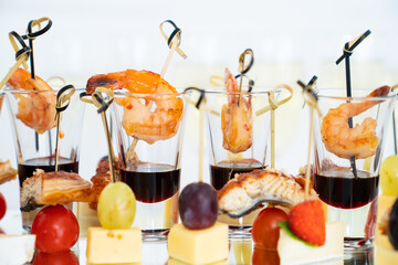 canapes of cheese with fruit, fish with tomatoes and shrimp with sauce in glass.