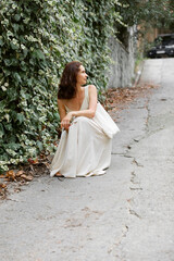 A cute smiling 40-year-old woman in linen dress with reusable bag against the background of a green wall of leaves  in autumn. The concept of naturalness, freedom, pleasure of life, eco friendly.