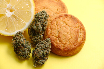 Cookies with CBD oil. Marijuana buds on yellow background. Cannabis blooms and lemon cookies close-up. Top view, flat lay.