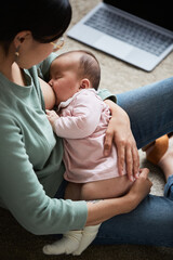 Young woman feeding her sleeping baby with breast sitting in the room