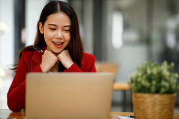 Happy excited successful Asian young businesswoman triumphing with laptop at modern office