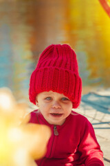 A small kid in the autumn in the park cries in a red warm hat and sweater.