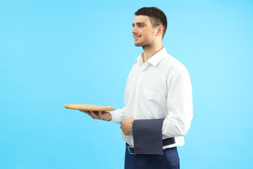 Young man waiter holds tray and towel on blue background