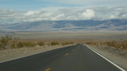 Fototapeta premium Road trip to Death Valley, driving auto in California, USA. Hitchhiking traveling in America. Highway, mountains and dry desert, arid climate wilderness. Passenger POV from car. Journey to Nevada.