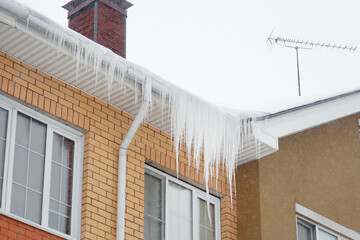 Big icicles on the roof of a townhouse on a snowy winter day among thaw