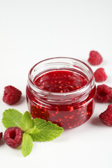 Jar of raspberry jam with ingredients on white background