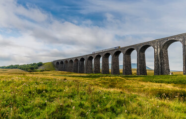 A view of a train on the middle of the Ribblehead Viaduct, Yorkshire, UK in summertime