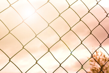Fototapeta premium The texture of the metal mesh-netting against the background of the pastel colors of the sky. Beautiful abstract background.