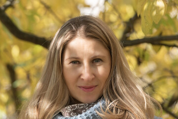 Fototapeta premium Portrait of a beautiful young blonde girl in a blue coat in an autumn park, close-up.