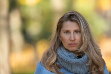 Naklejka premium Portrait of a beautiful young blonde girl in a blue coat in an autumn park, close-up.