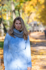 Portrait of a beautiful young blonde girl in a blue coat in an autumn park, close-up.