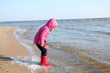Child girl playing by the sea in autumn.