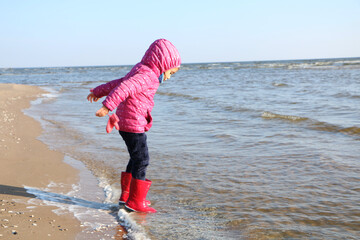 Child girl playing by the sea in autumn.