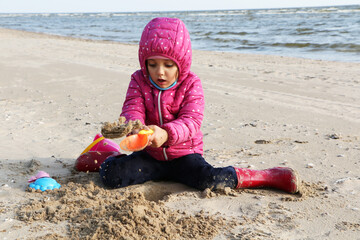 Girl playing in the sand on the beach in autumn.