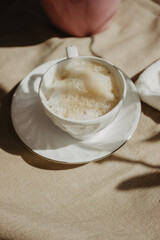 Modern coffee cup with milk and foam on a beige background isolated with a plant shadow.